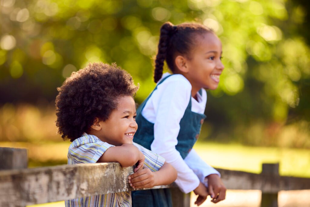 Two Smiling Children Leaning On Fence On Walk In Countryside